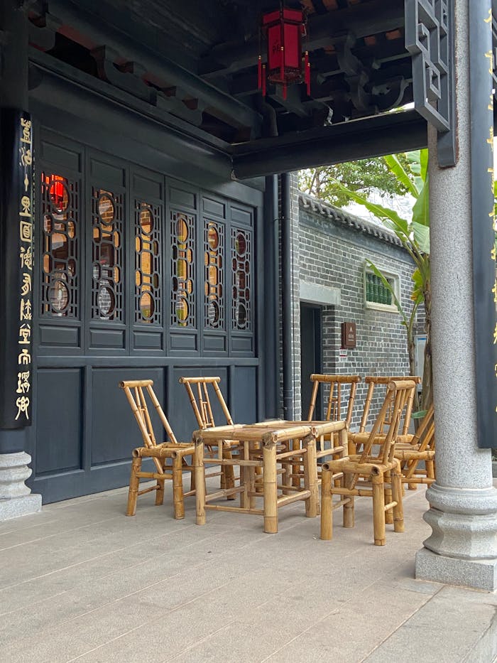 Elegant outdoor scene of a traditional Asian courtyard with bamboo furniture and intricate architecture.